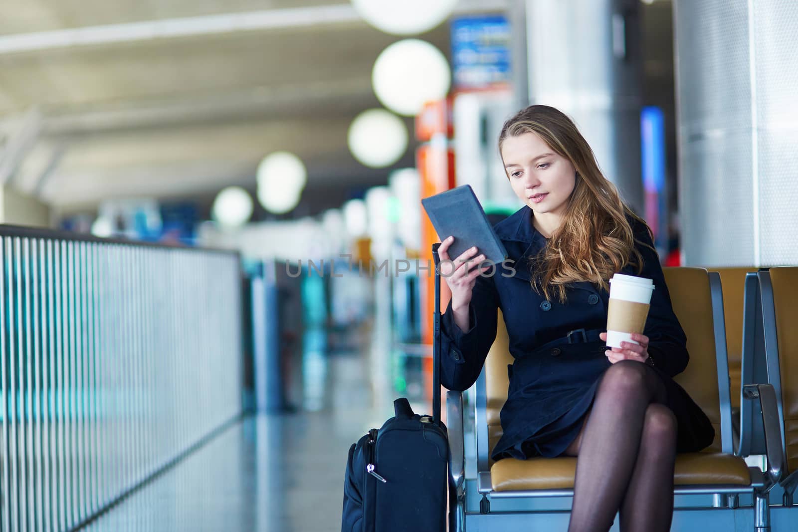 Young woman in international airport, reading and drinking coffee while waiting for her flight