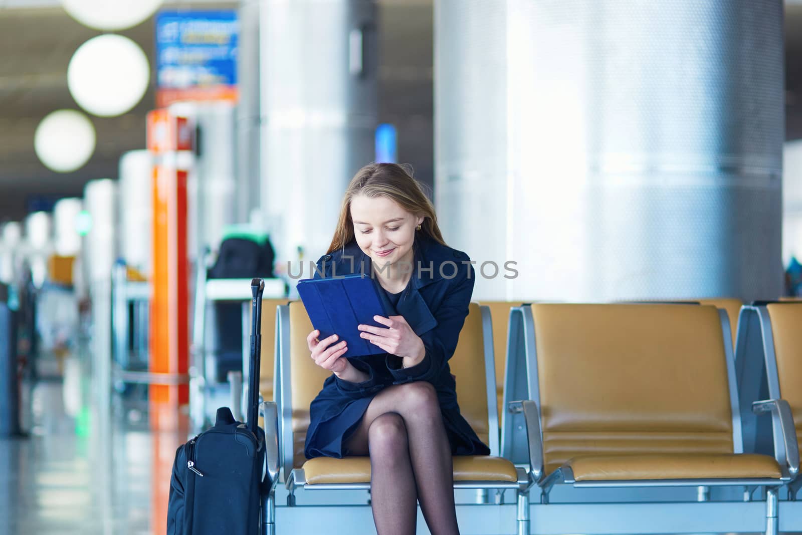 Young woman in international airport, waiting for her flight, using her tablet