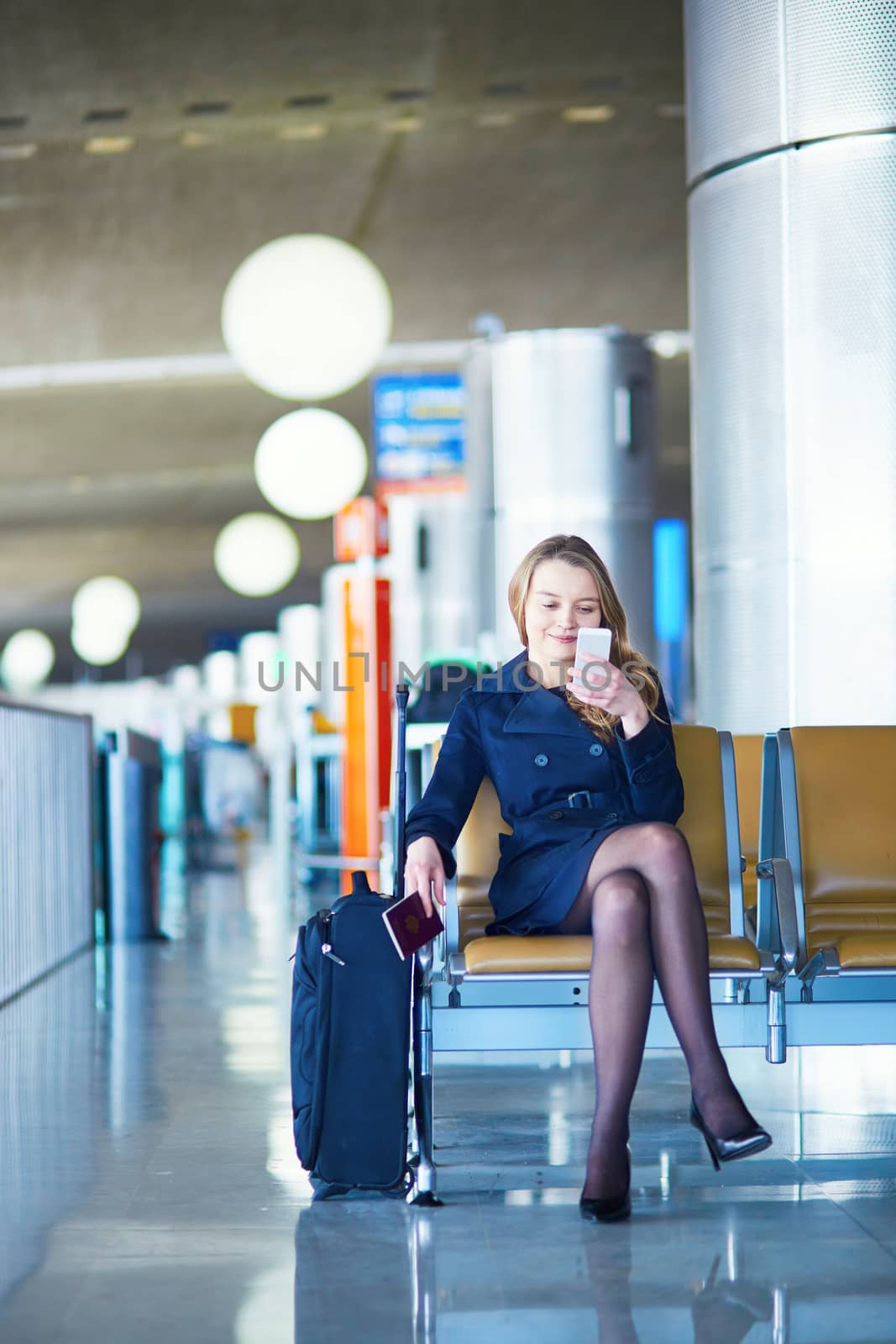 Young woman in international airport, waiting for her flight, using her mobile phone