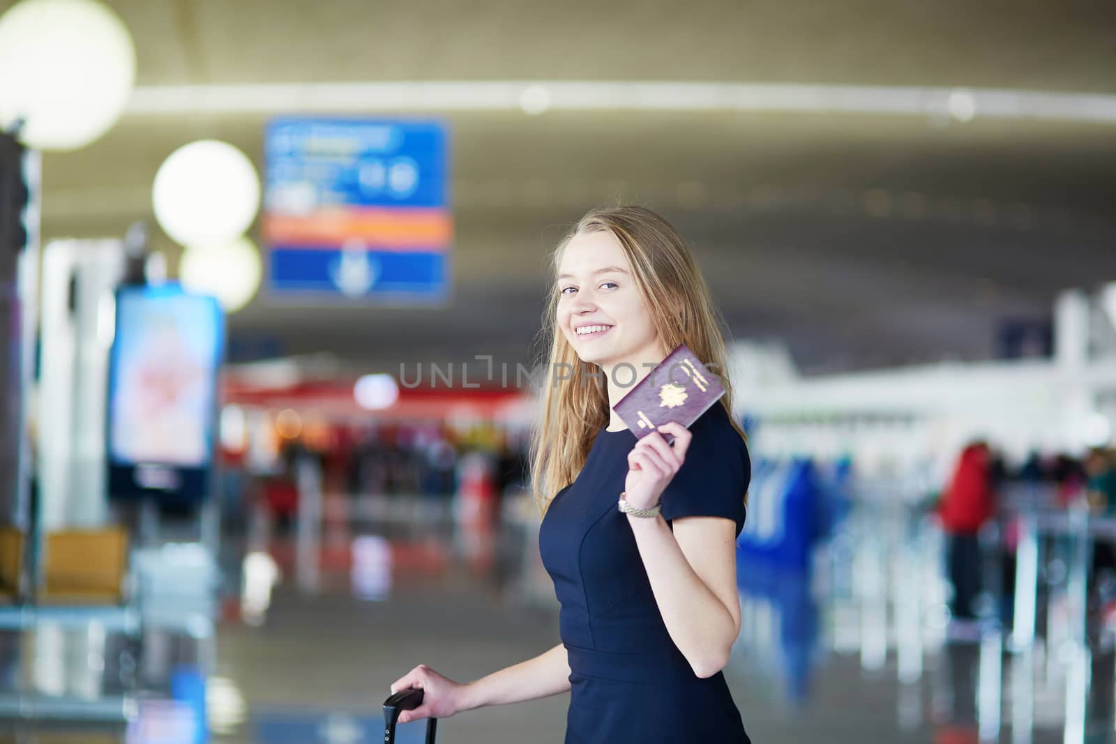 Young woman in international airport, holding French passport and looking happy