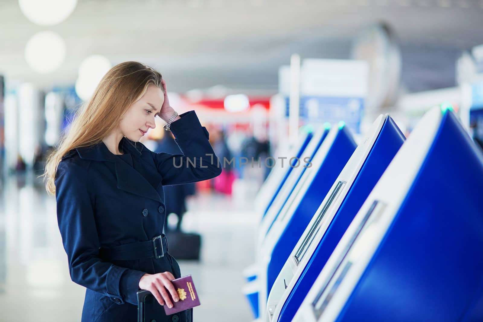 Young woman in international airport doing self check-in, stressed and concerned. Missed, delayed or canceled flight concept