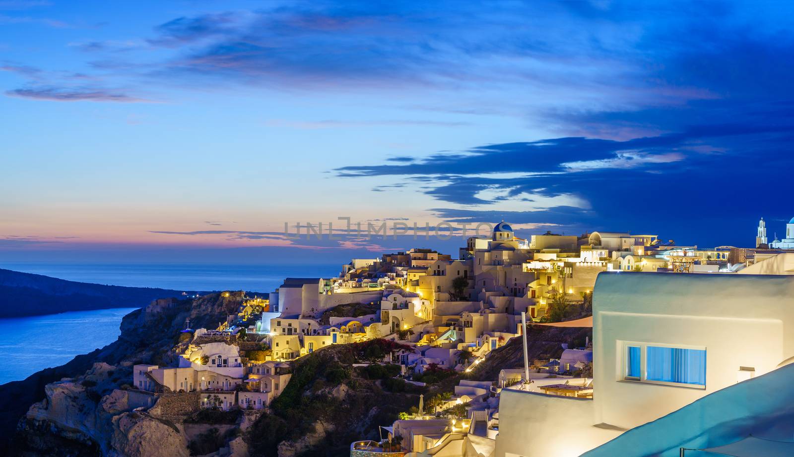 Picturesque view, Old Town of Oia or Ia on the island Santorini, white houses, windmills and church with blue domes at sunset, Greece