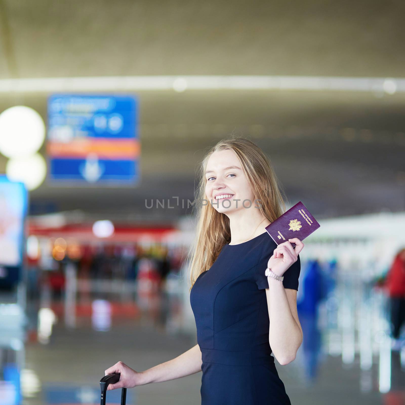 Young woman in international airport, holding French passport and looking happy