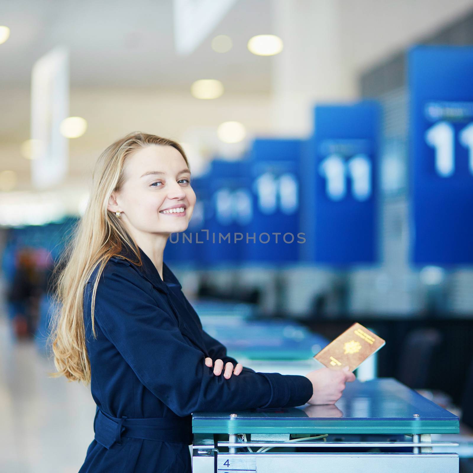 Young woman in international airport at check-in counter, giving her passport to an officer and waiting for her boarding pass