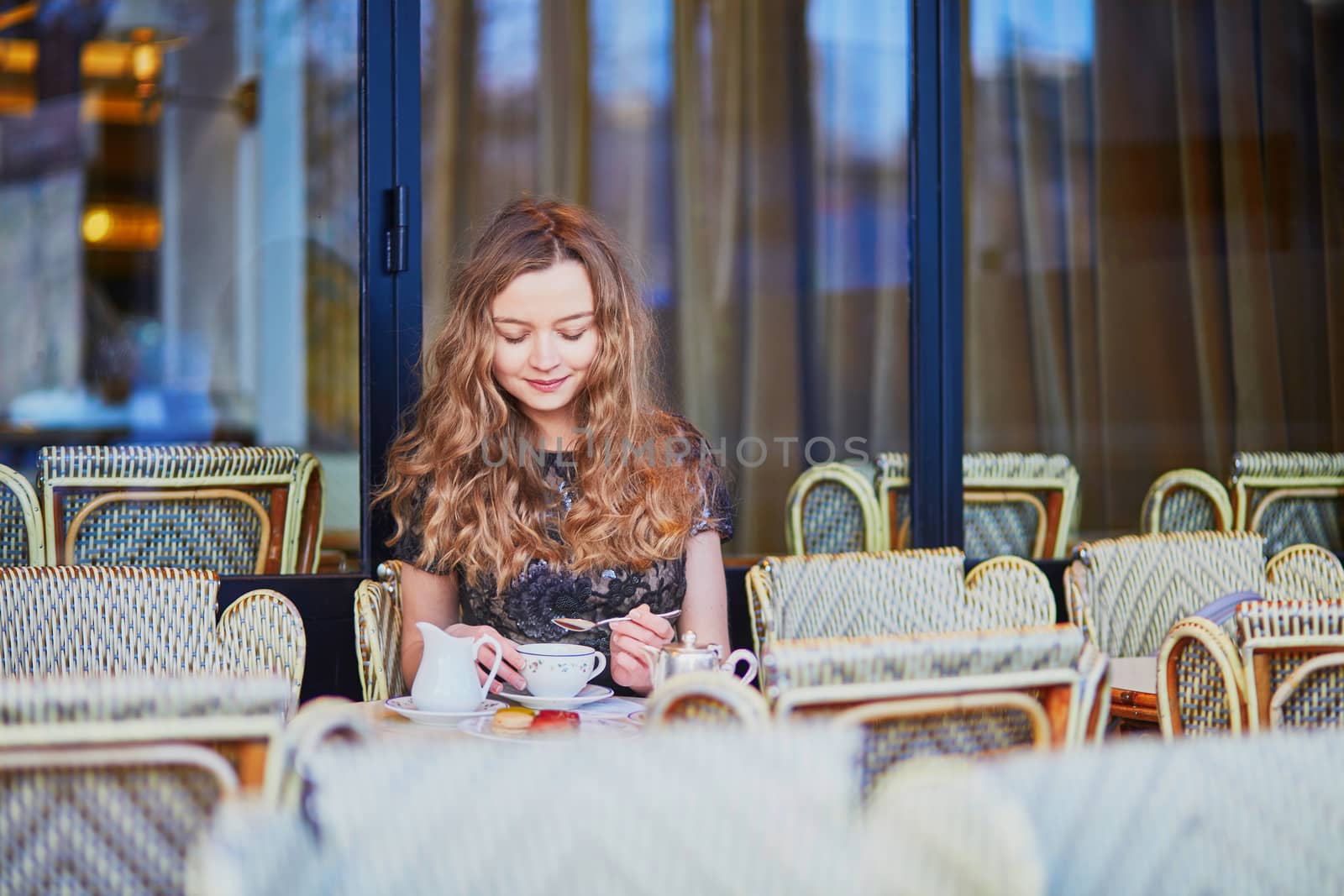 Beautiful Parisian woman in cafe, drinking coffee and eating macaroons, traditional French dessert