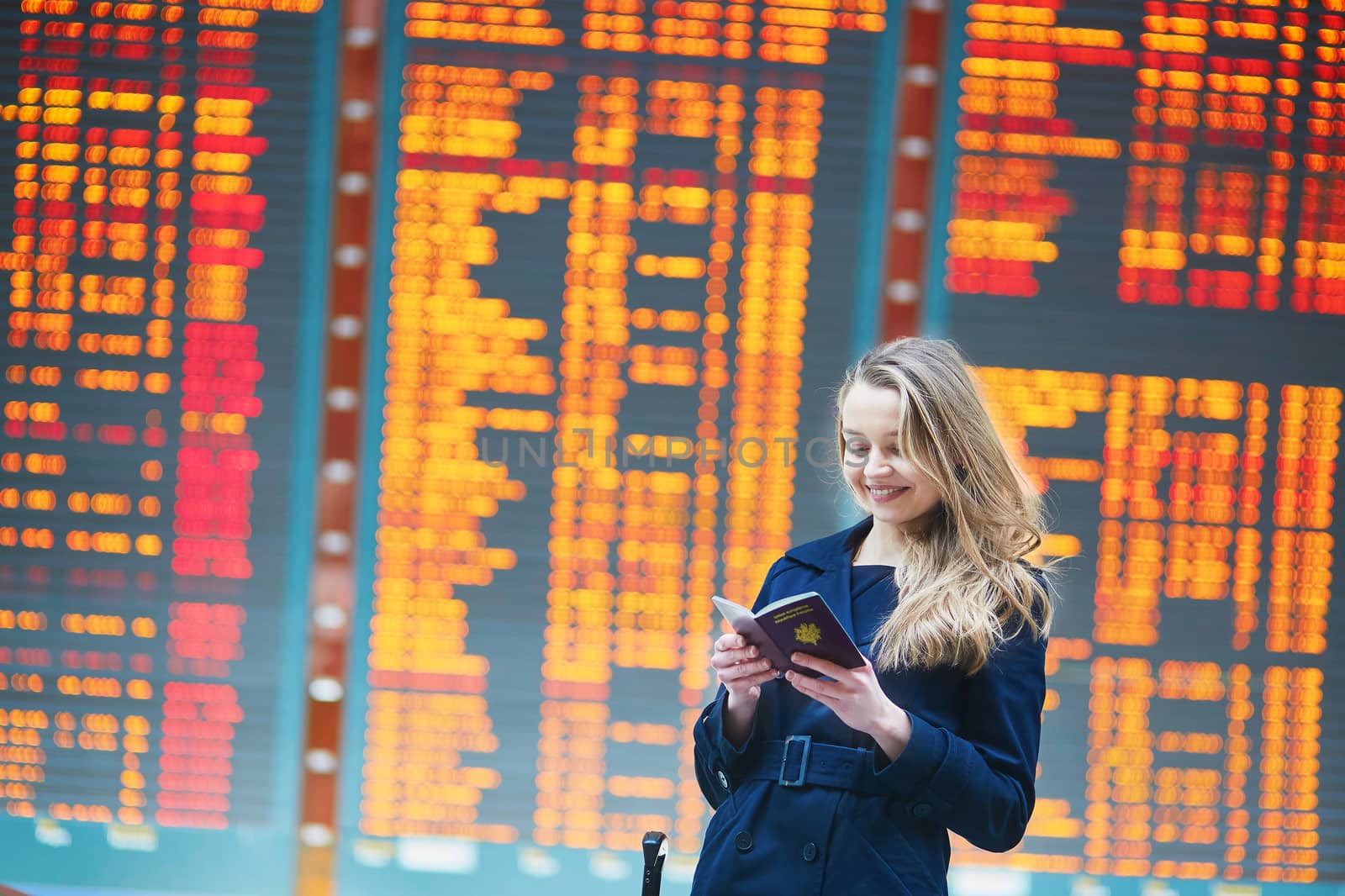 Young woman in international airport near the flight information board, checking her passport