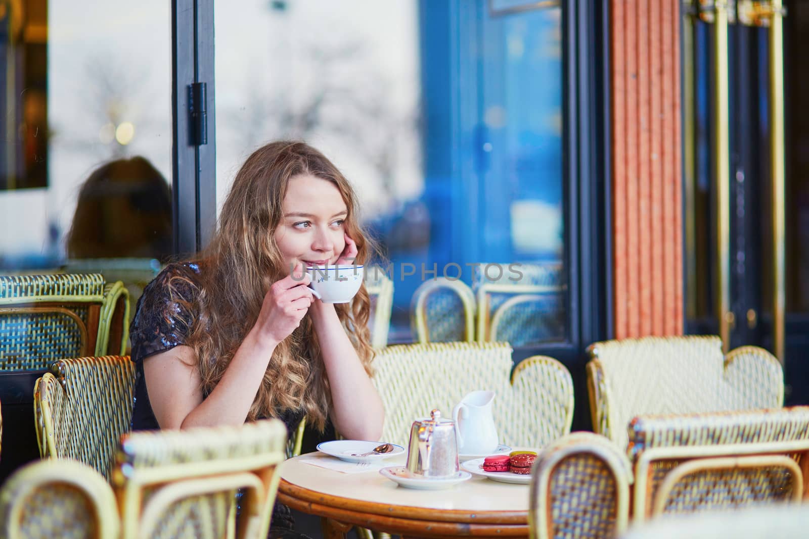 Beautiful Parisian woman in cafe, drinking coffee and eating macaroons, traditional French dessert