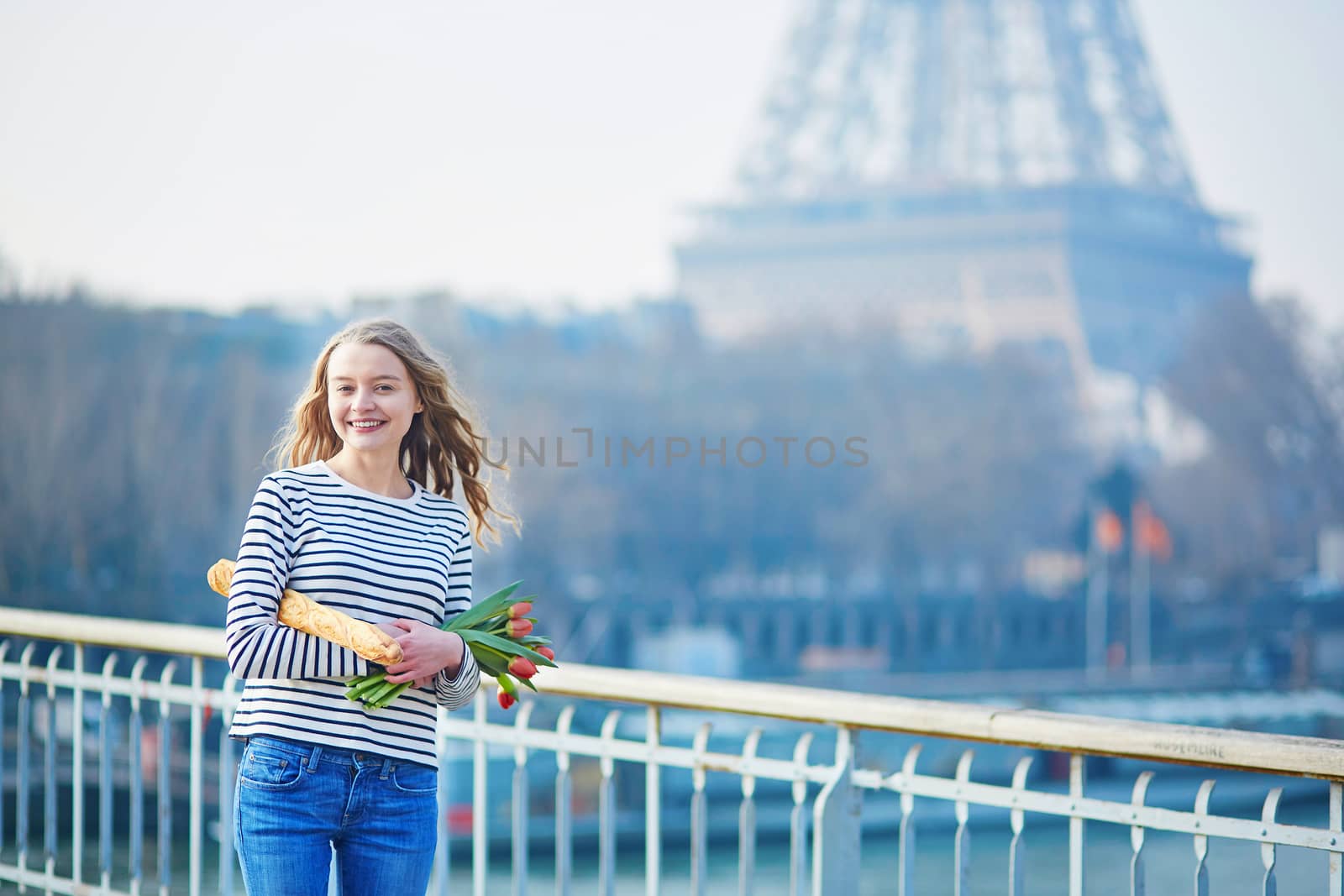 Beautiful young girl with fresh tasty traditional French bread (baguette) and tulips near the Eiffel tower