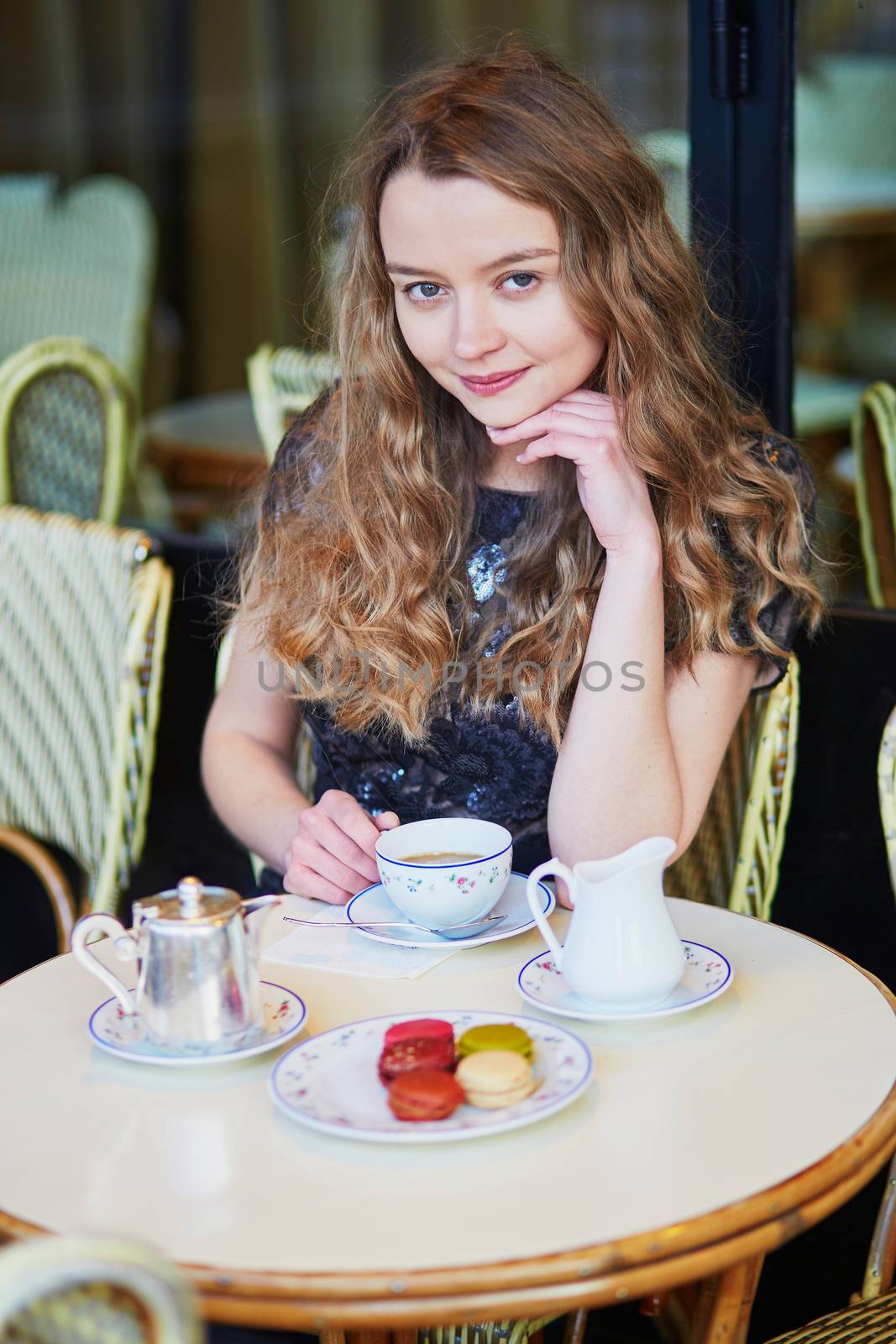 Beautiful Parisian woman in cafe, drinking coffee and eating macaroons, traditional French dessert
