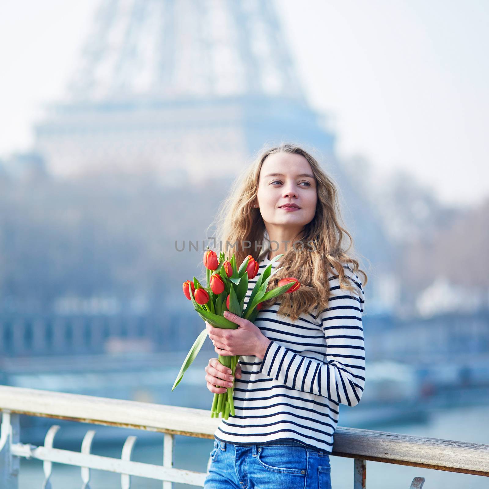 Beautiful young girl with bunch of red tulips near the Eiffel tower in Paris, France on a clear spring day