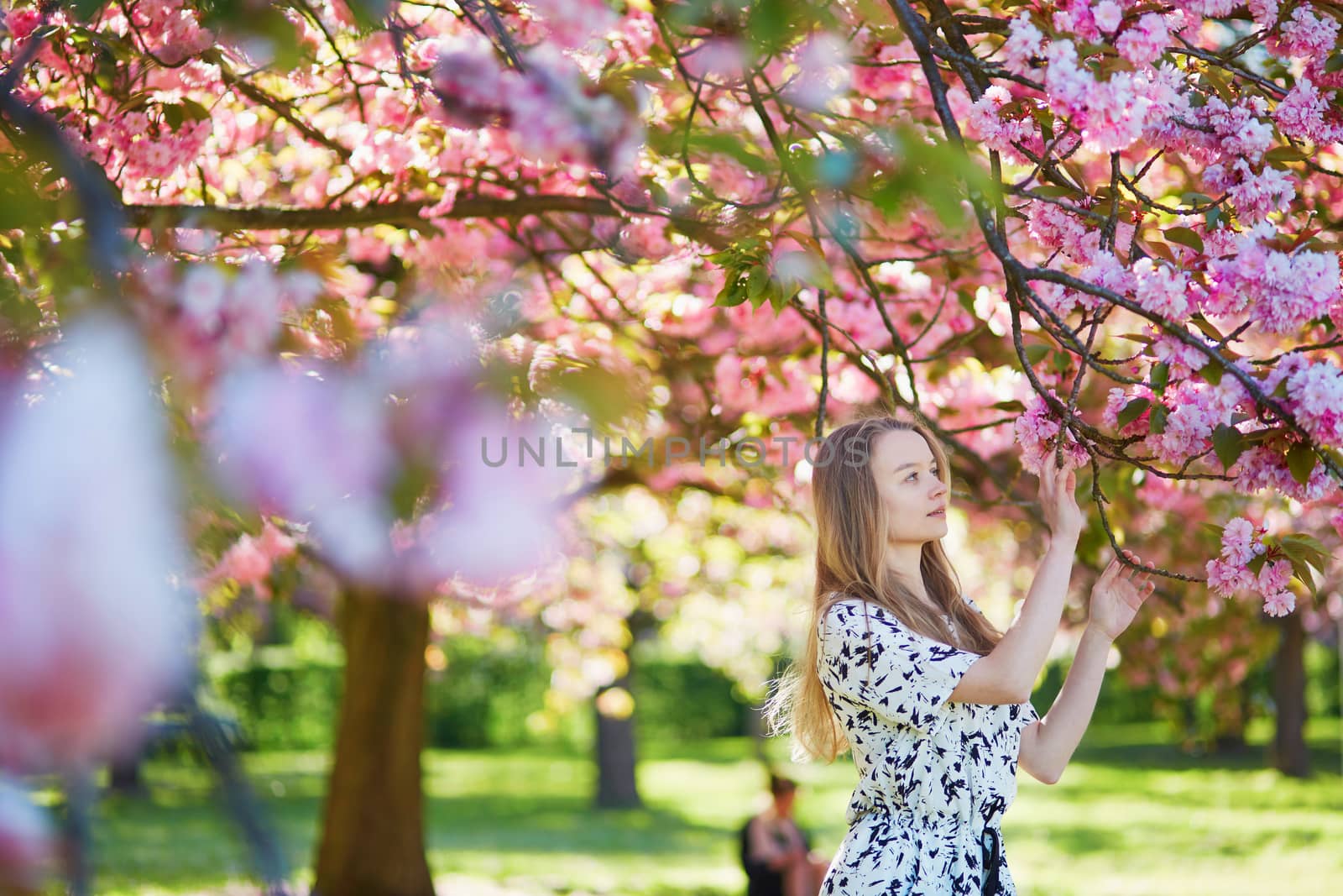 Beautiful young woman enjoying sunny day in park during cherry blossom season on a nice spring day