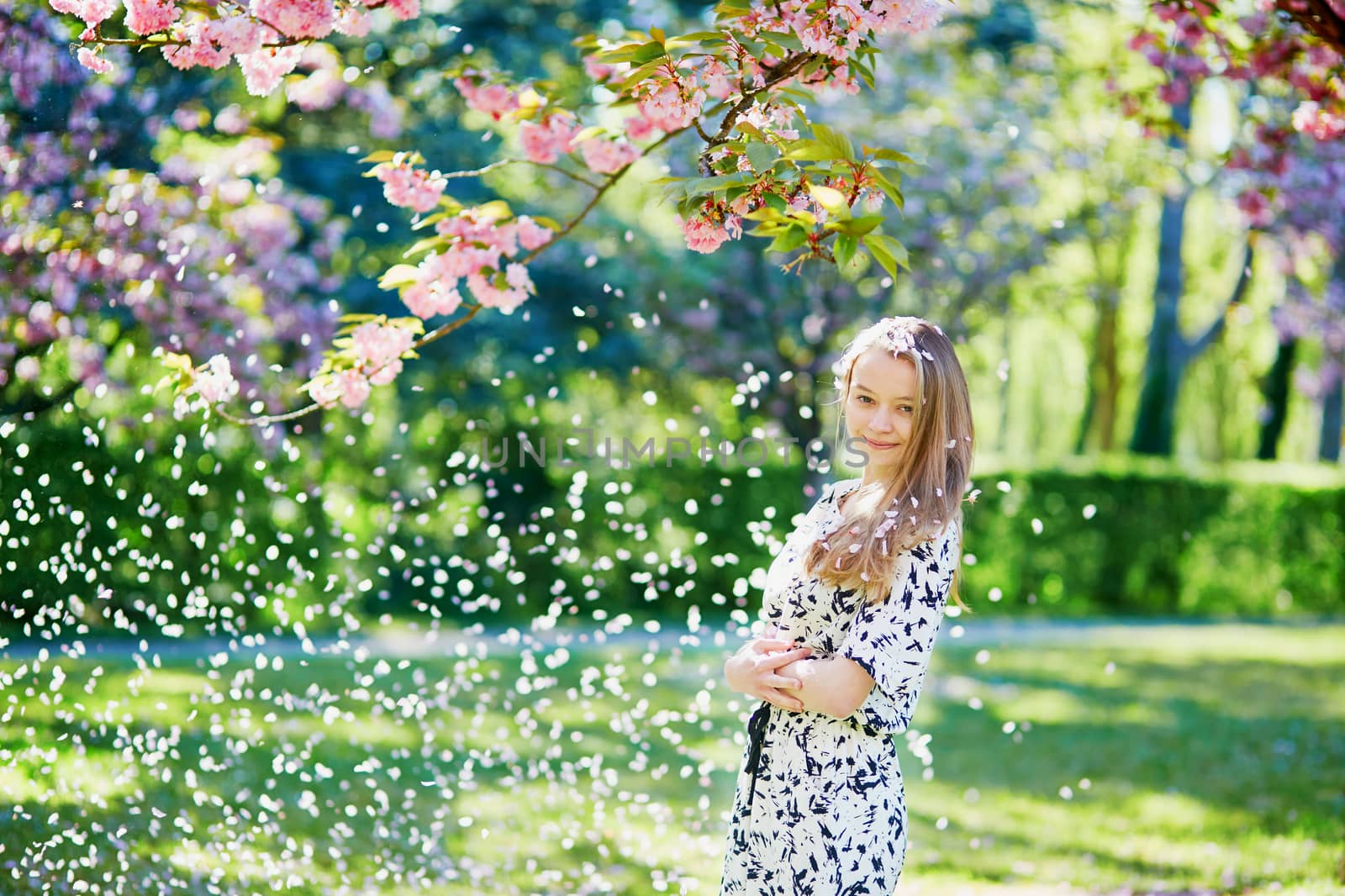 Beautiful young woman enjoying sunny day in park during cherry blossom season on a nice spring day