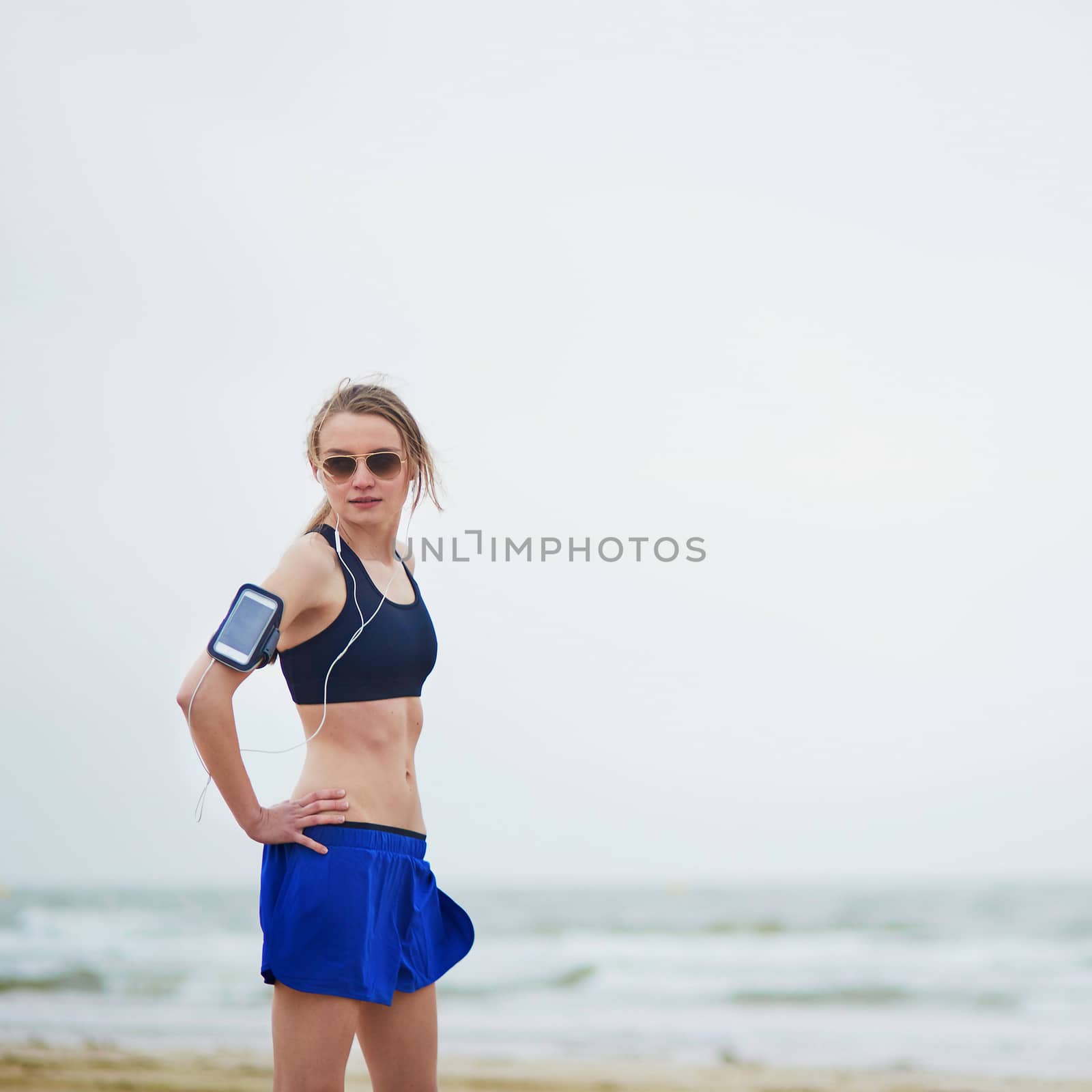 Running fitness woman wearing phone armband monitor tracker. Jogger running on beach and listening to music using earphones