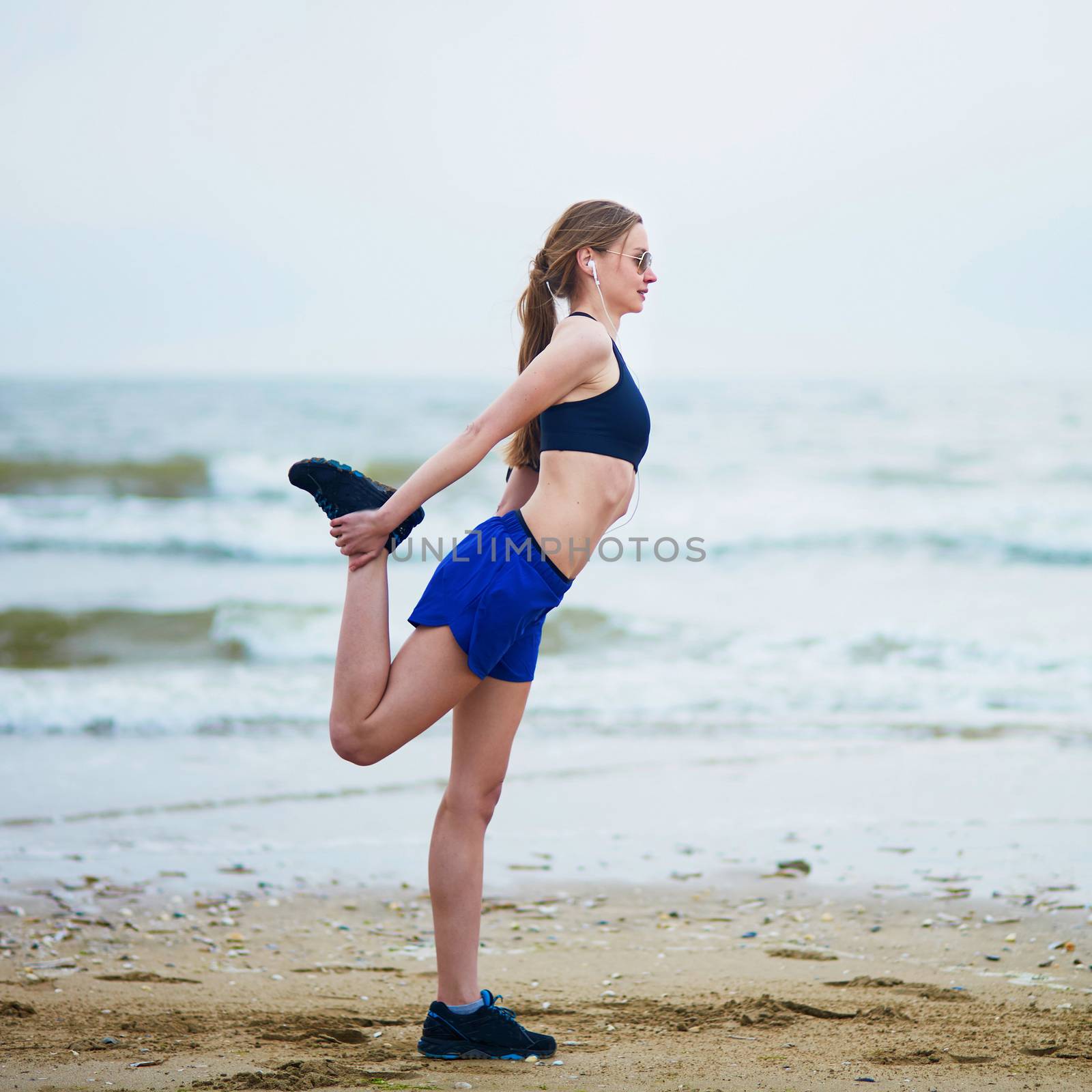 Young fitness running woman stretching on beach by jaspe