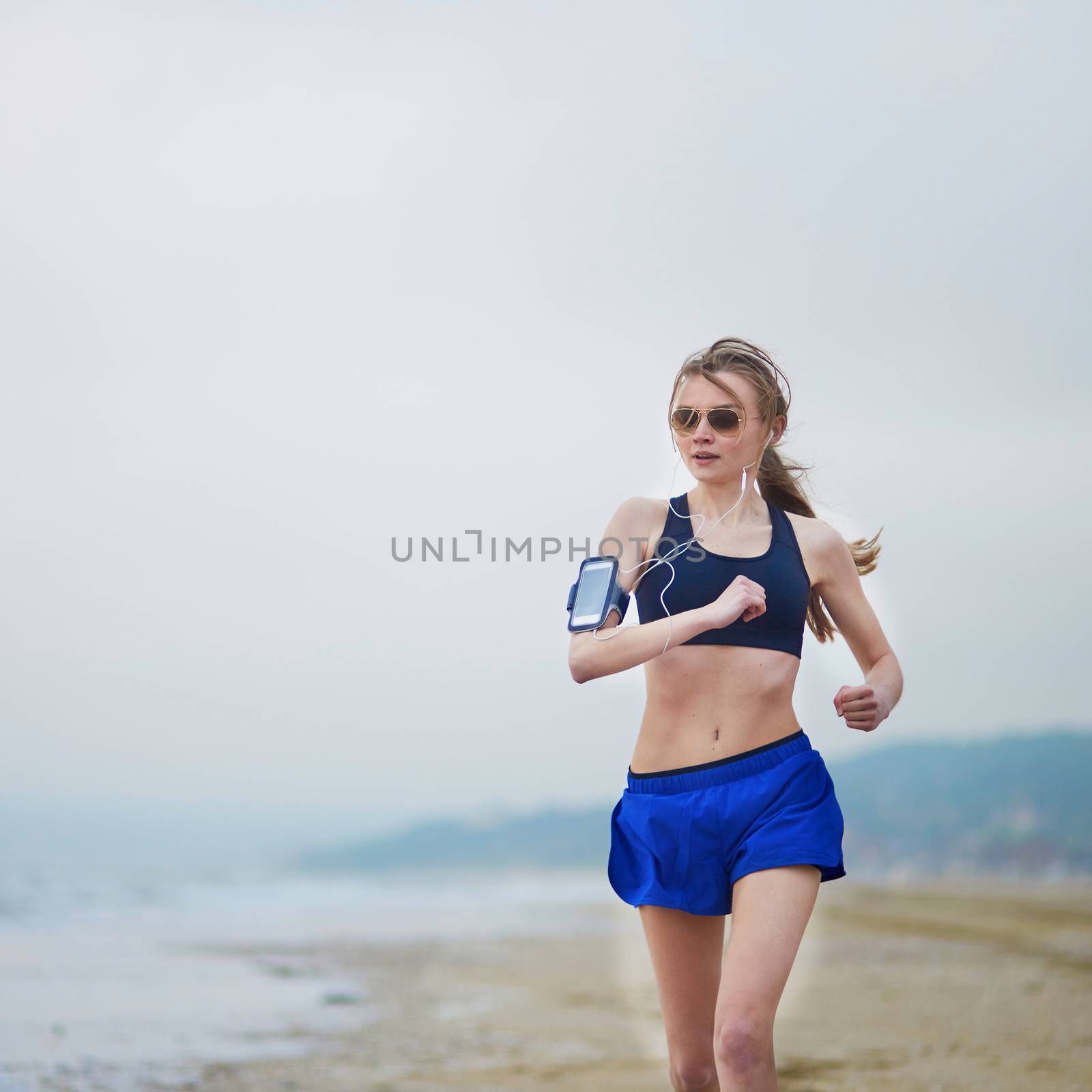 Young fitness running woman jogging on beach by jaspe