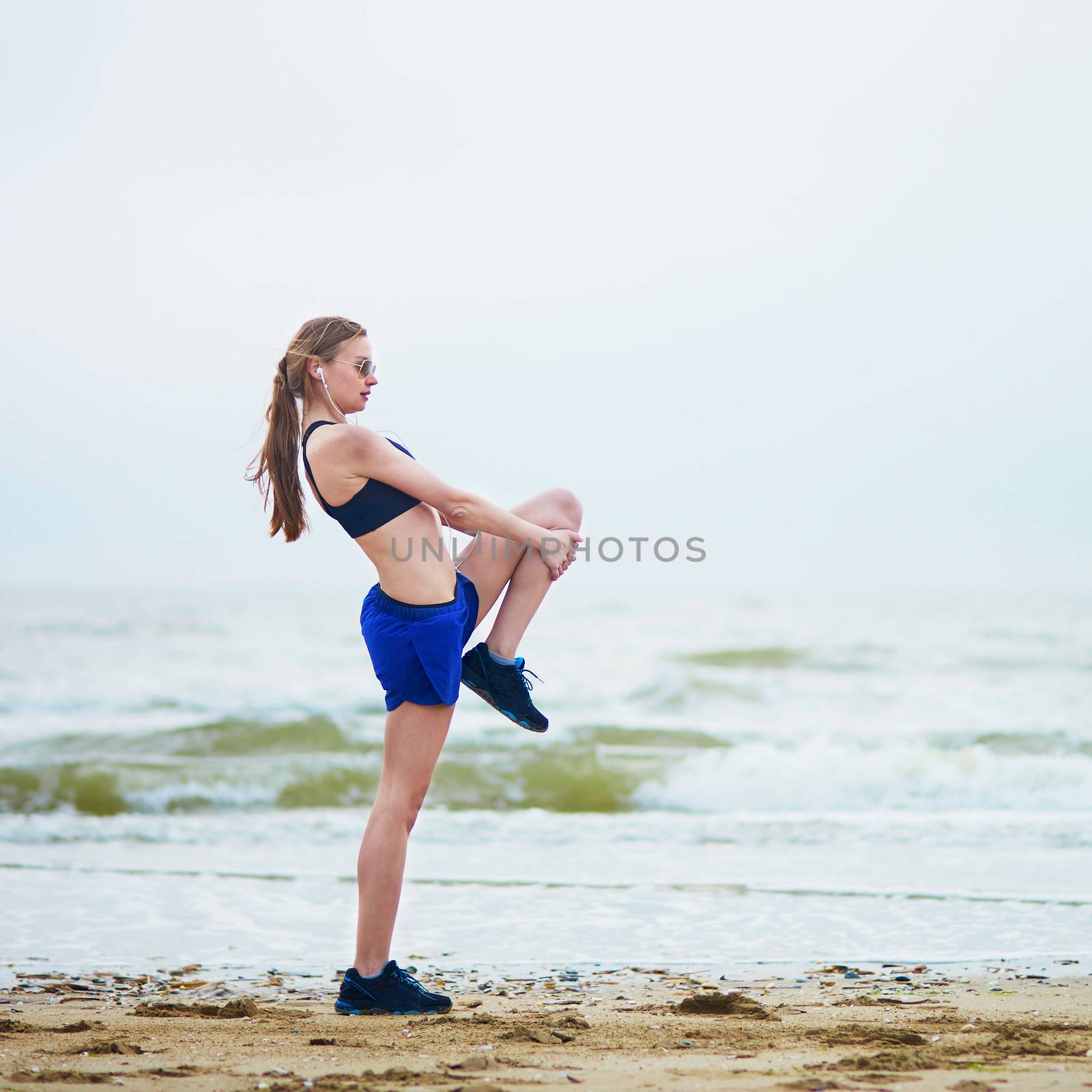 Young fitness running woman stretching on beach by jaspe