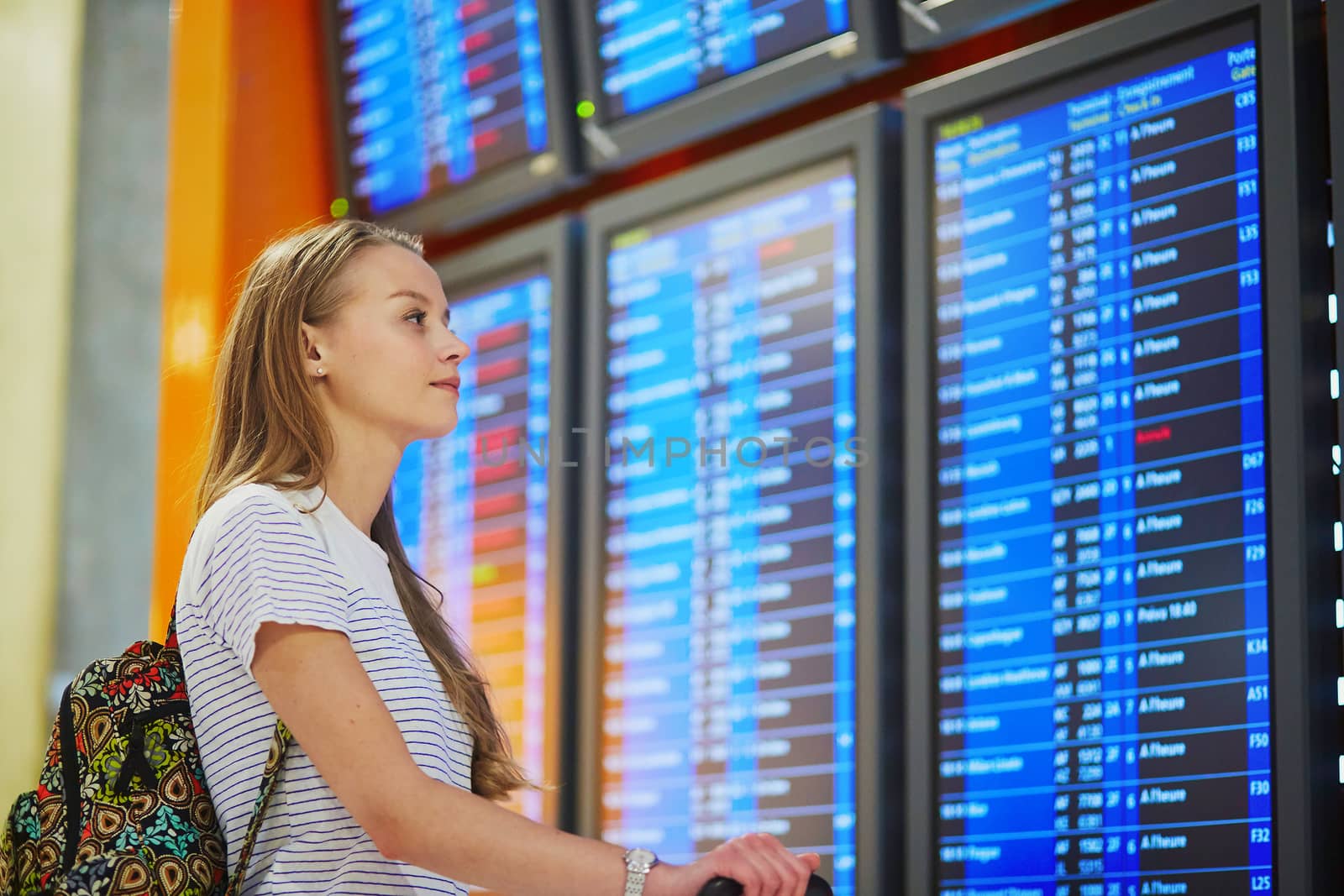 Young woman in international airport looking at the flight information board by jaspe