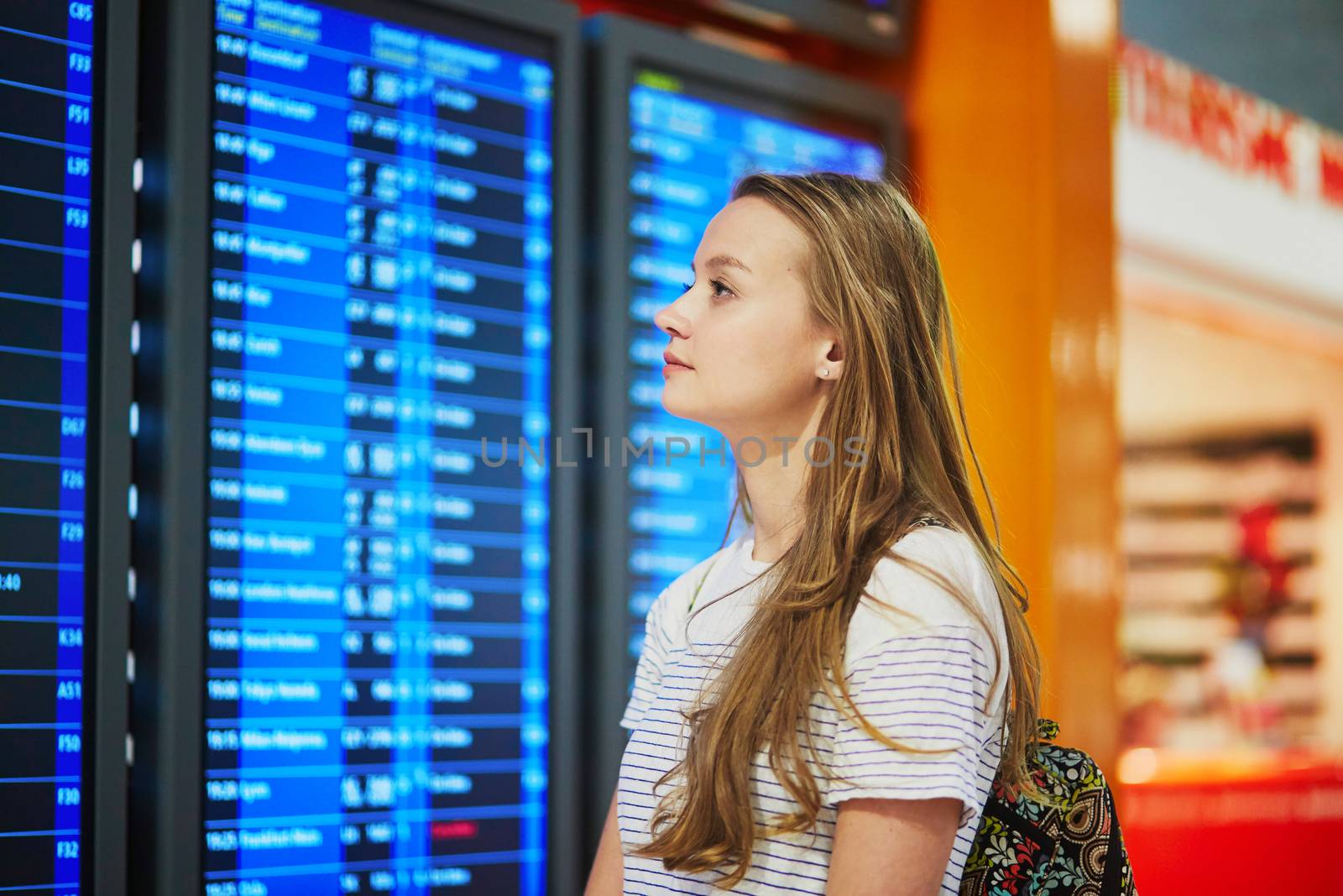 Young woman in international airport looking at the flight information board by jaspe