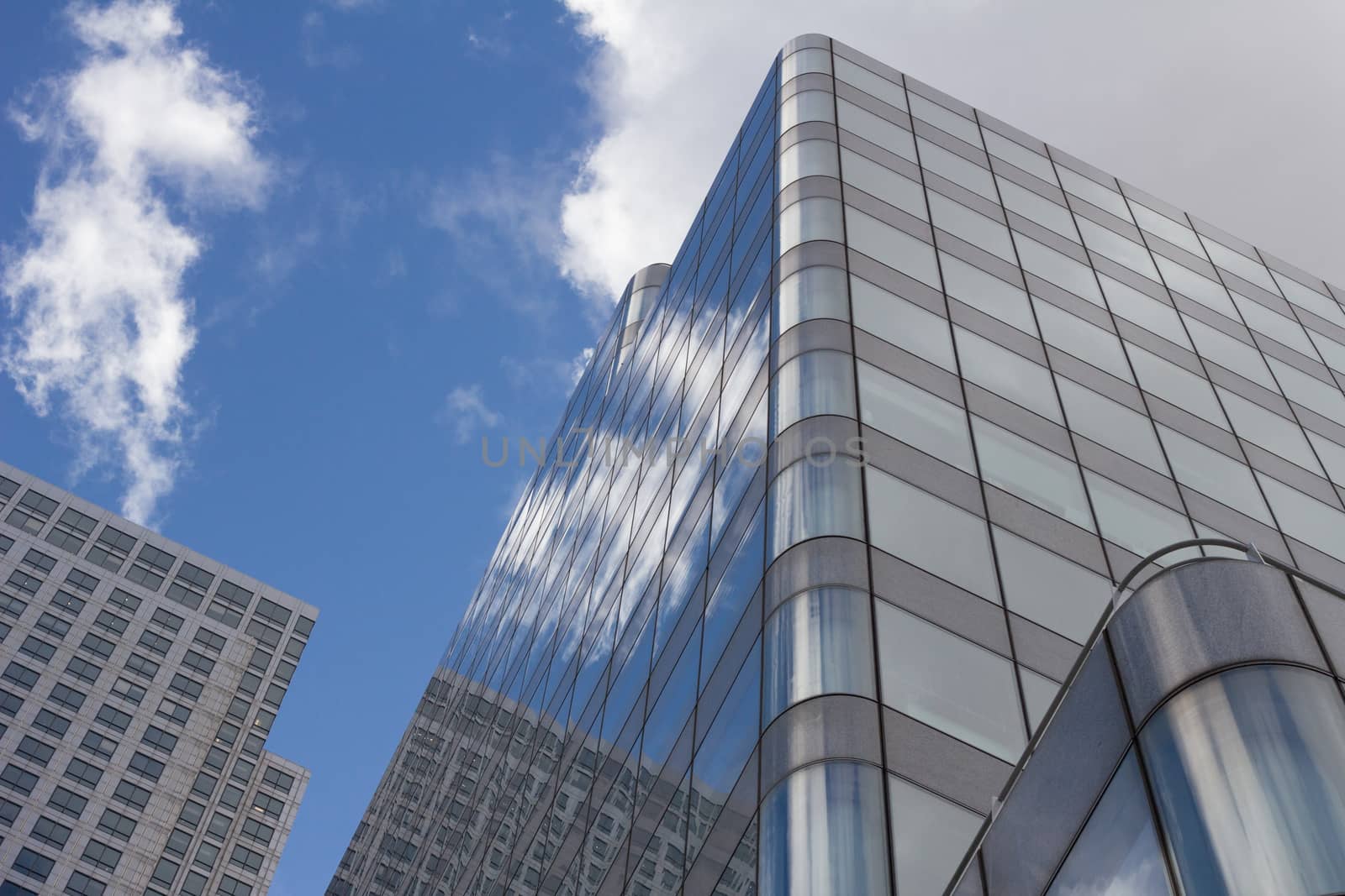 A modern glass exterior skyscraper reflecting the clouds and blue sky