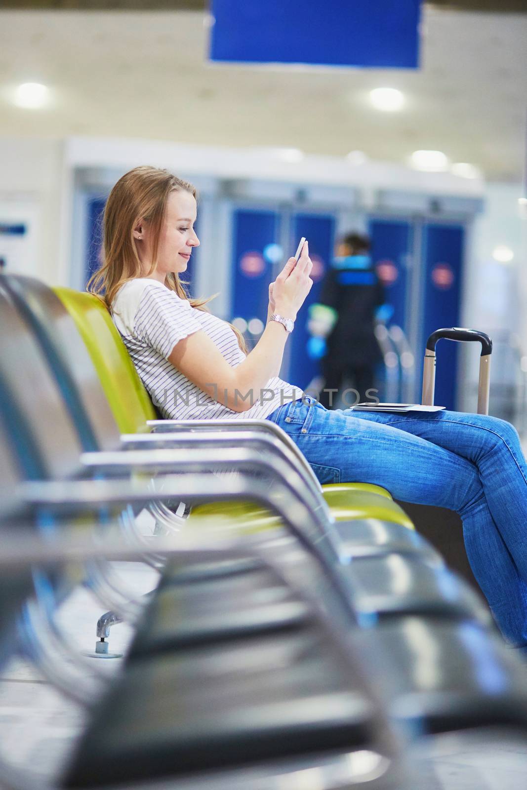 Young woman in international airport using mobile phone while waiting for her flight