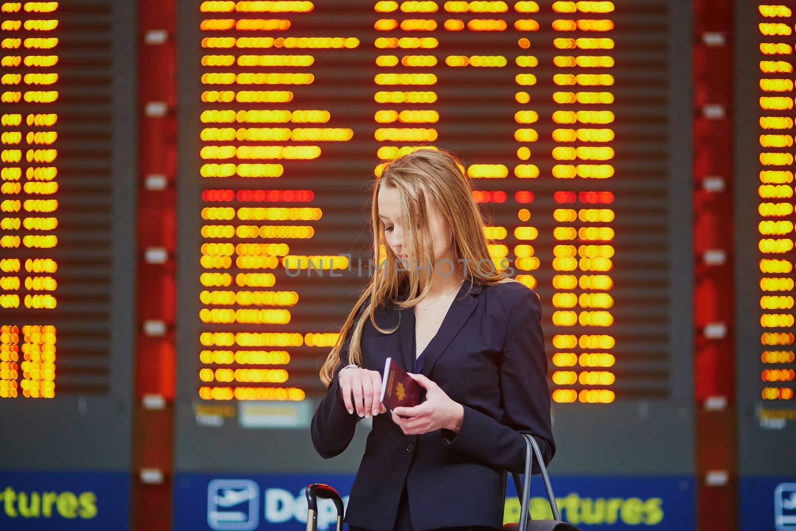 Young elegant business woman with hand luggage in international airport terminal, looking at information board, checking her flight. Cabin crew member with suitcase.