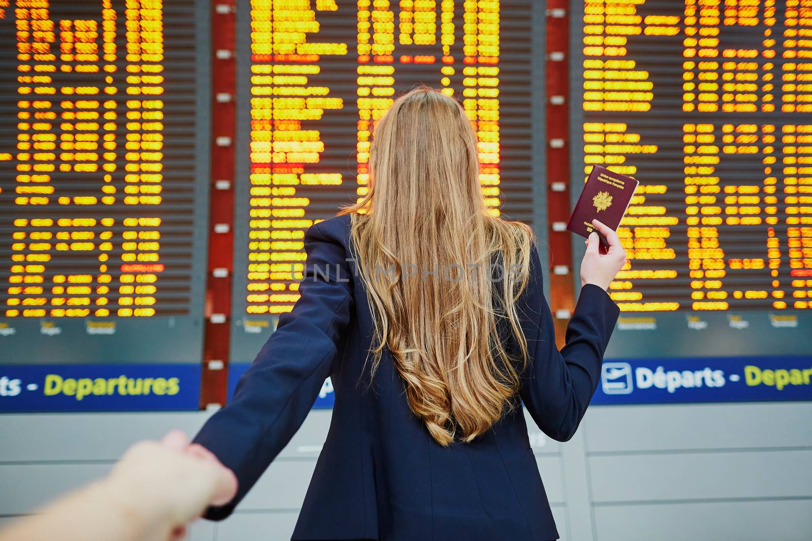 Young elegant business woman looking at information board, checking her flight, in the international airport. Follow me concept