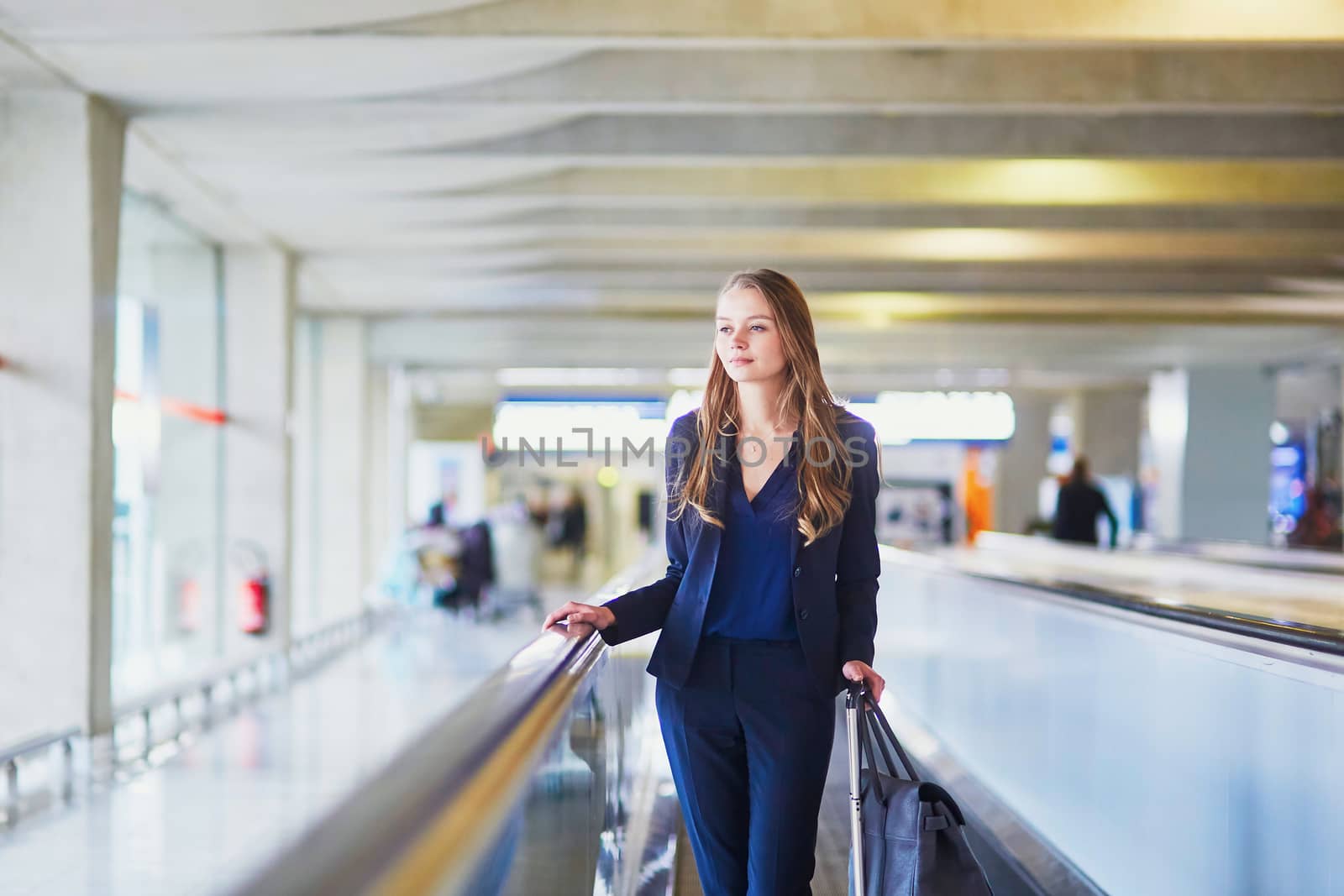 Young elegant woman with hand luggage on travelator on international airport terminal. Cabin crew member with suitcase. Travel or business trip concept