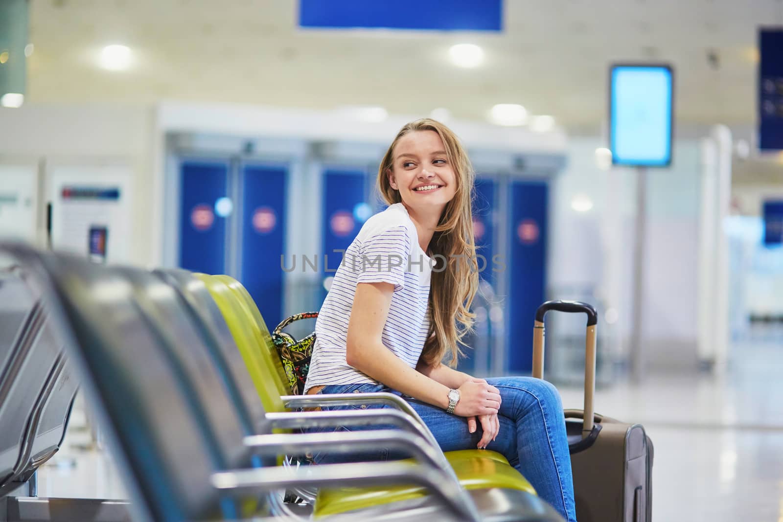 Beautiful young tourist girl with backpack and carry on luggage in international airport, waiting for flight