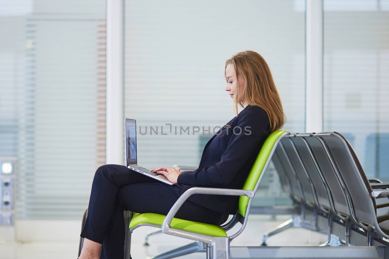 Young woman in international airport working on laptop while waiting for her flight