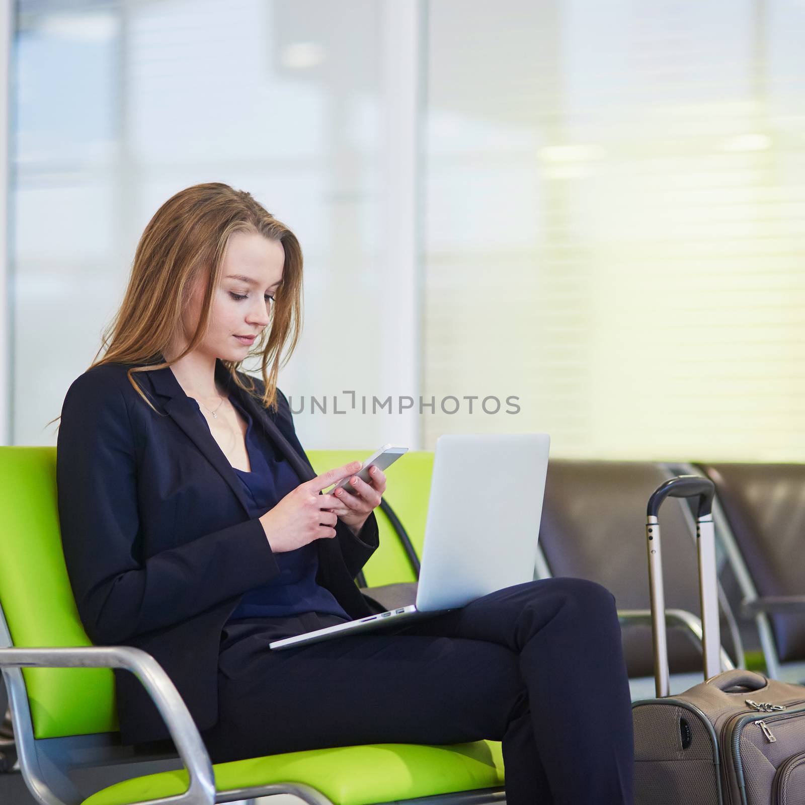 Young woman in international airport working on laptop while waiting for her flight