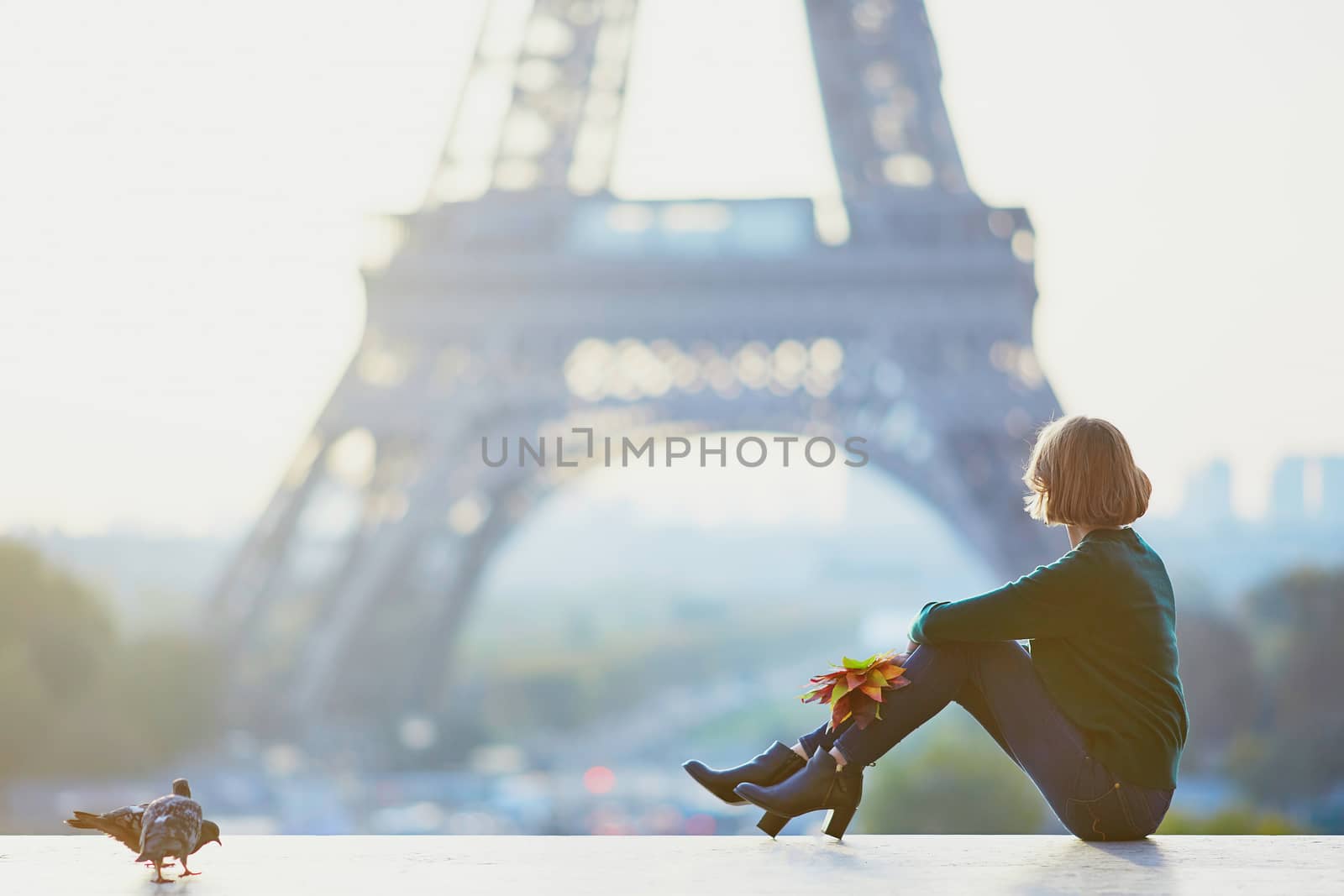 Beautiful young French woman with bunch of colorful autumn leaves near the Eiffel tower in Paris on a fall day