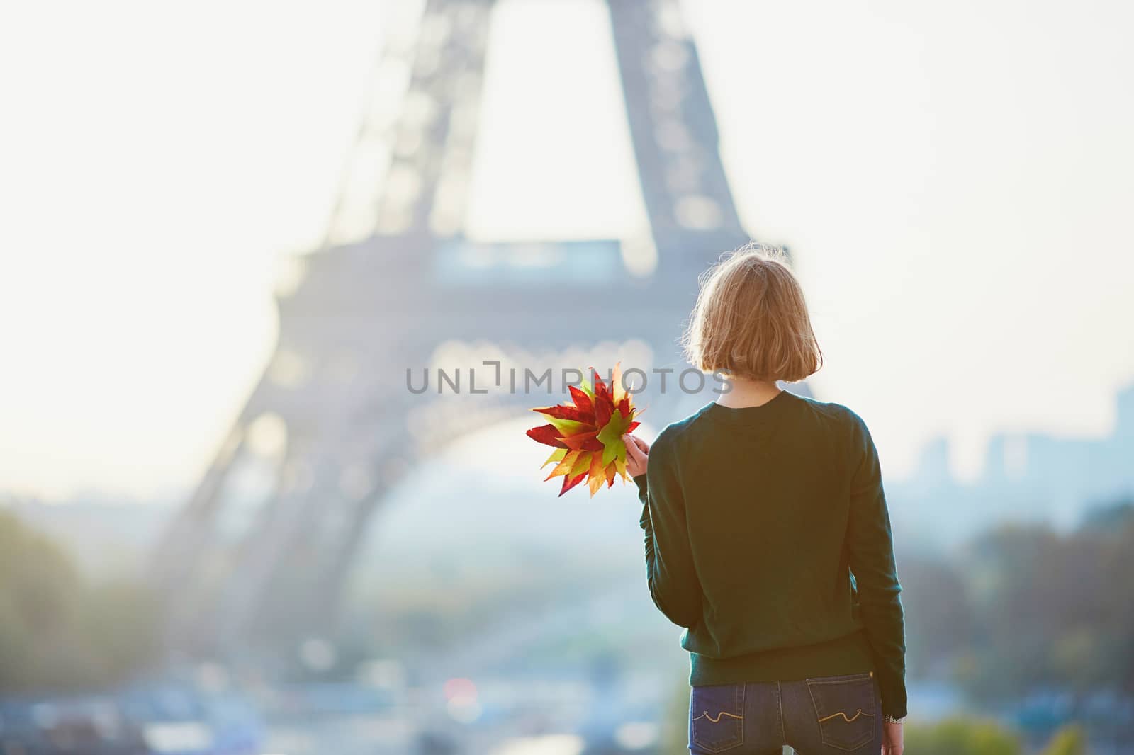 Beautiful young French woman with bunch of colorful autumn leaves near the Eiffel tower in Paris on a fall day