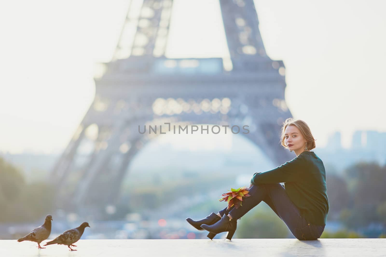 Beautiful young French woman with bunch of colorful autumn leaves near the Eiffel tower in Paris on a fall day