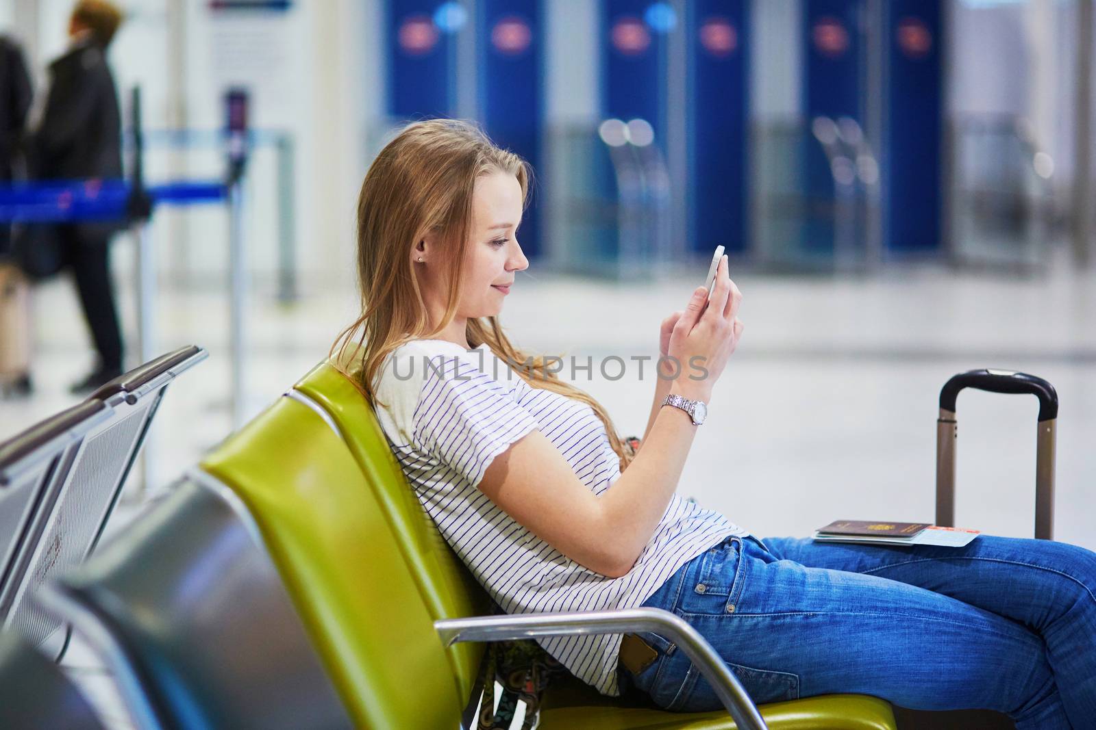 Young woman in international airport using mobile phone while waiting for her flight
