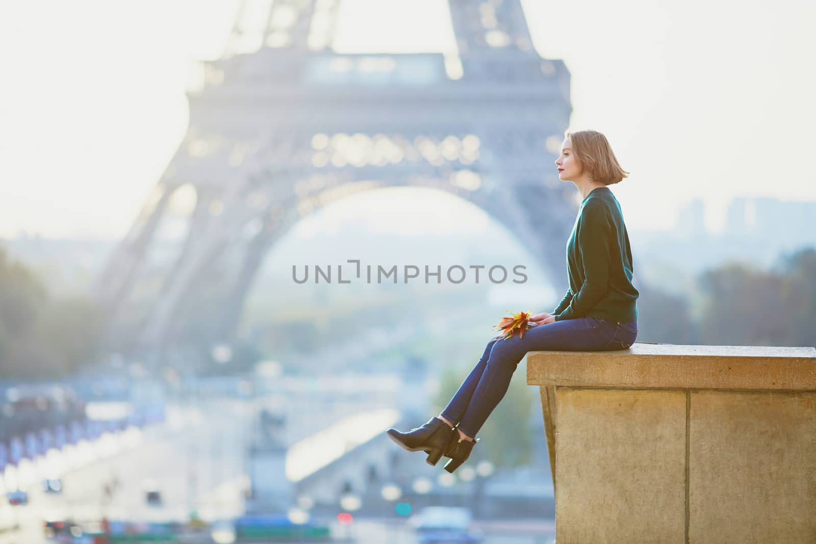 Beautiful young French woman with bunch of colorful autumn leaves near the Eiffel tower in Paris on a fall day