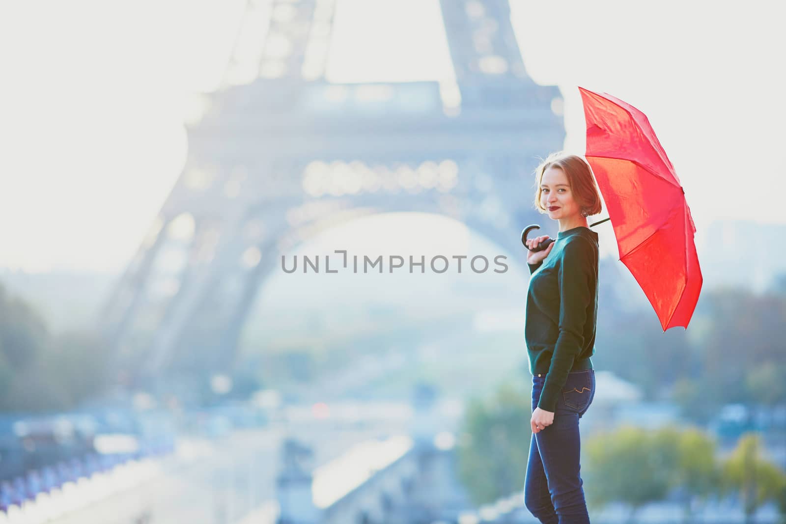 Beautiful young girl with red umbrella in Paris near the Eiffel tower at morning