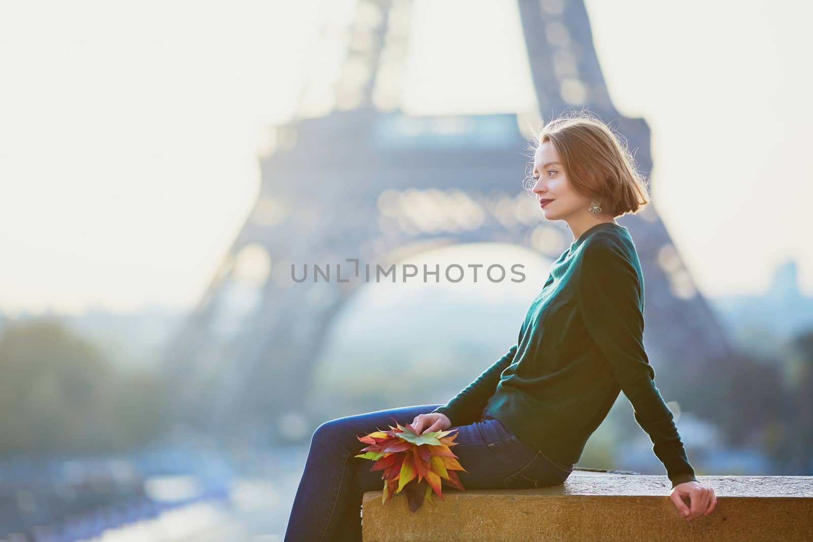 Beautiful young French woman with bunch of colorful autumn leaves near the Eiffel tower in Paris on a fall day