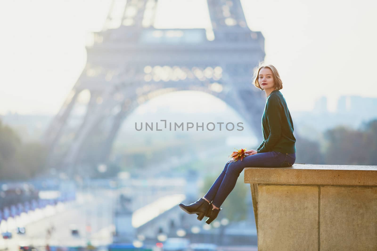 Beautiful young French woman with bunch of colorful autumn leaves near the Eiffel tower in Paris on a fall day