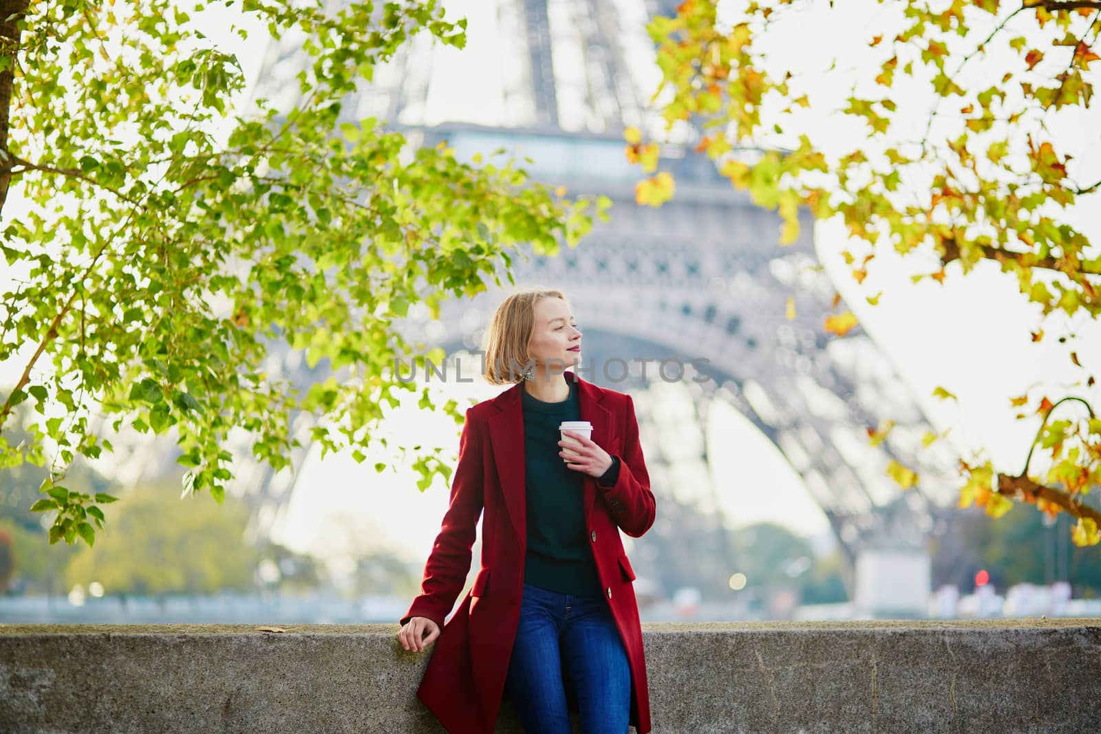 Beautiful young French woman with bunch of colorful autumn leaves near the Eiffel tower in Paris on a fall day