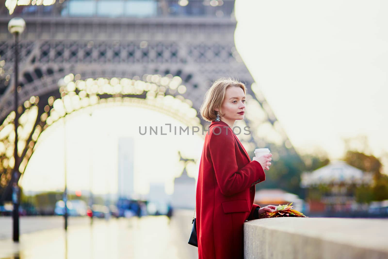 Beautiful young French woman drinking coffee near the Eiffel tower in Paris on a fall or spring day