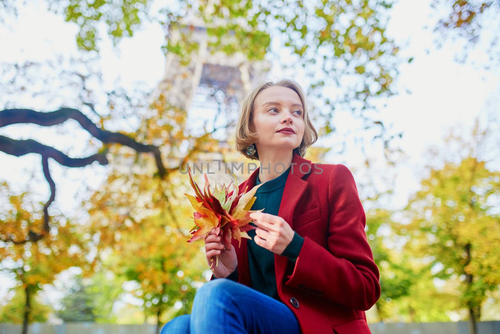 Beautiful young French woman with bunch of colorful autumn leaves near the Eiffel tower in Paris on a fall day