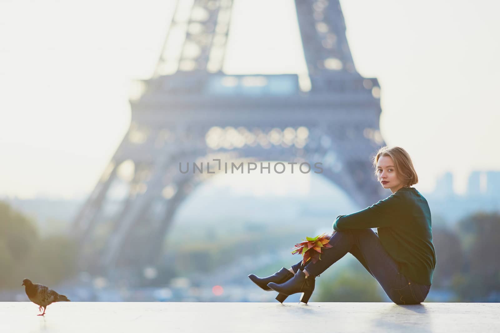 Beautiful young French woman with bunch of colorful autumn leaves near the Eiffel tower in Paris on a fall day