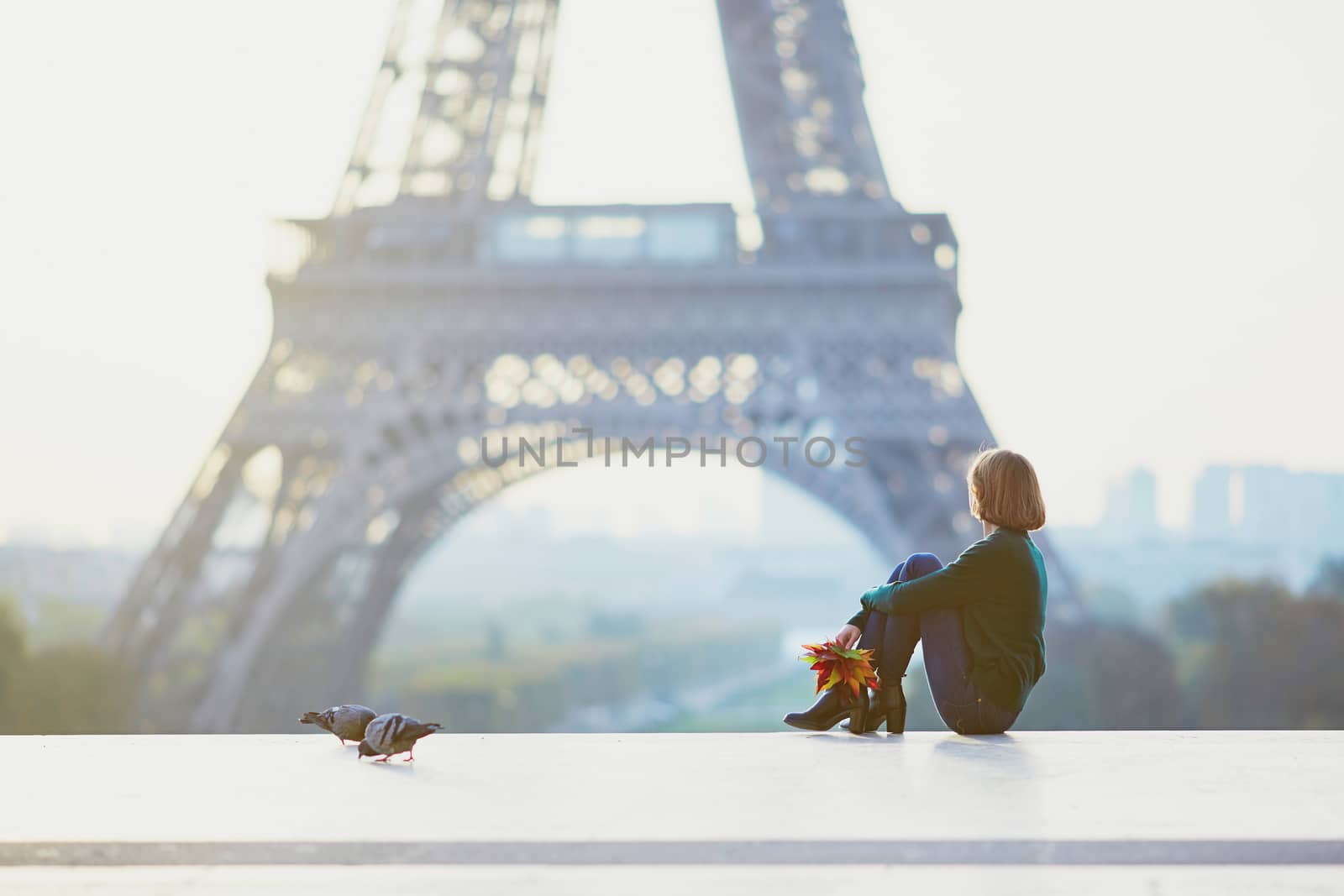 Beautiful young French woman with bunch of colorful autumn leaves near the Eiffel tower in Paris on a fall day