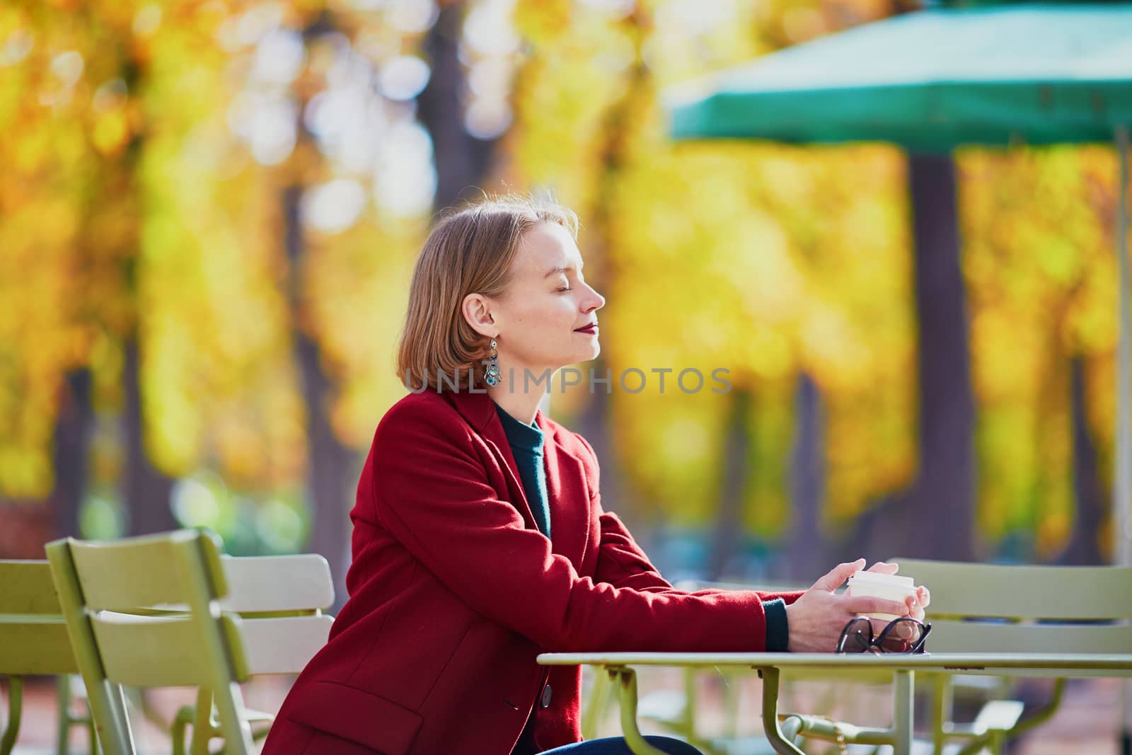 Elegant Parisian woman drinking coffee in park on a bright sunny autumn day