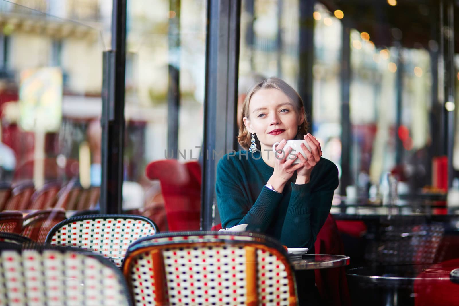 Elegant French woman drinking coffee in Parisian cafe near the window
