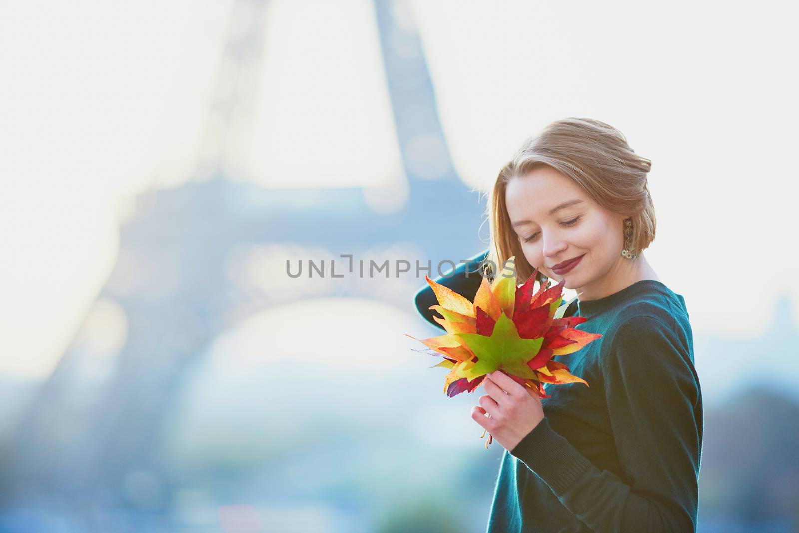 Beautiful young French woman with bunch of colorful autumn leaves near the Eiffel tower in Paris on a fall day