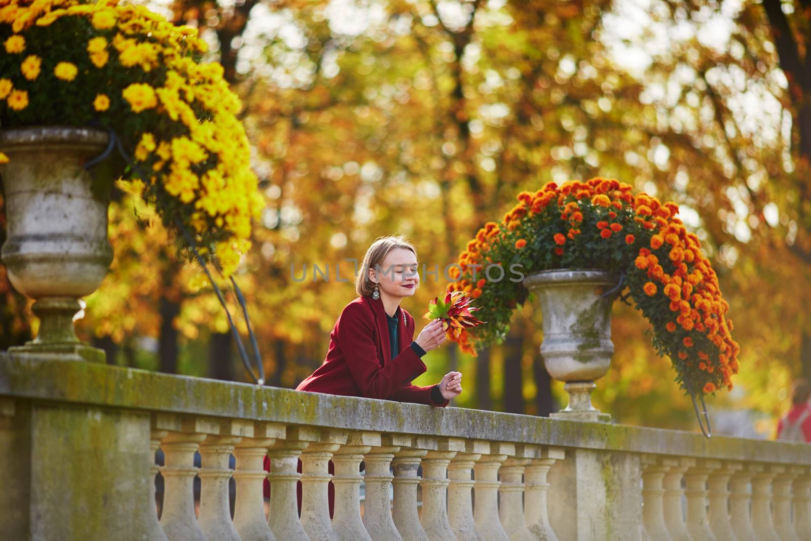 Beautiful young woman with bunch of colorful autumn leaves walking in park on a fall day. Luxembourg garden, Paris, France