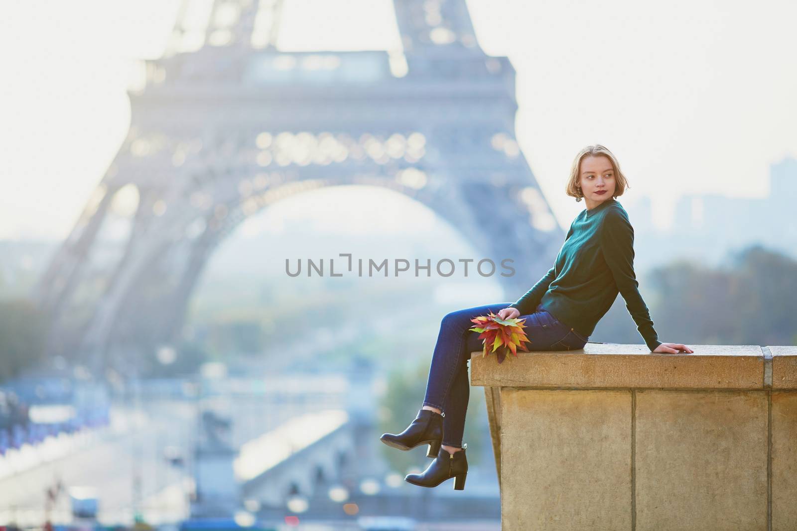Beautiful young French woman with bunch of colorful autumn leaves near the Eiffel tower in Paris on a fall day
