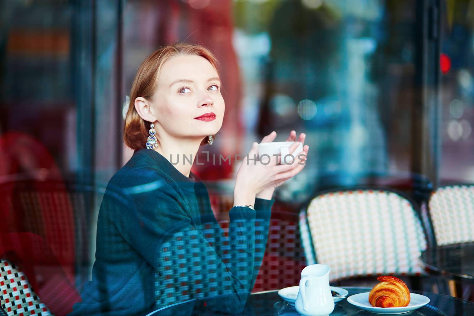 Elegant French woman drinking coffee in Parisian cafe near the window
