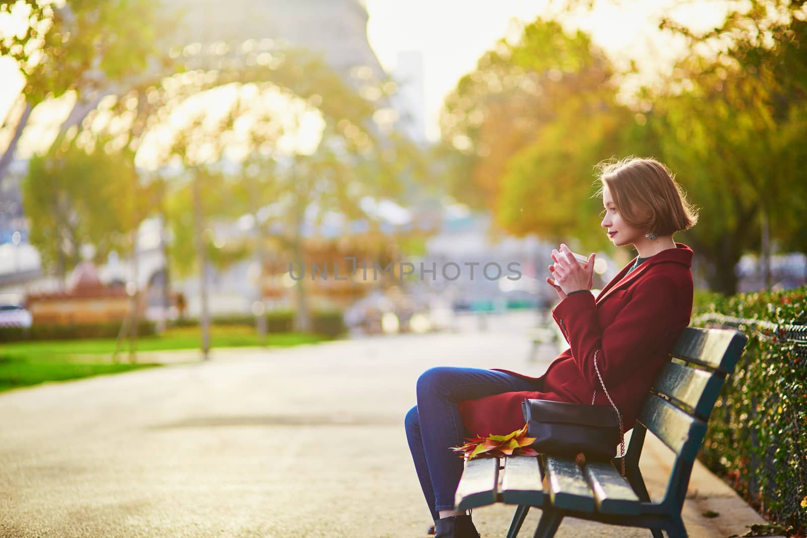 Beautiful young French woman with bunch of colorful autumn leaves sitting on the bench near the Eiffel tower in Paris on a fall day